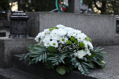 Photo of Funeral wreath of flowers on granite tombstone in cemetery