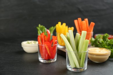 Photo of Celery and other vegetable sticks in glass bowls with dip sauce on black table