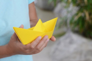 Photo of Little girl holding yellow paper boat outdoors, closeup