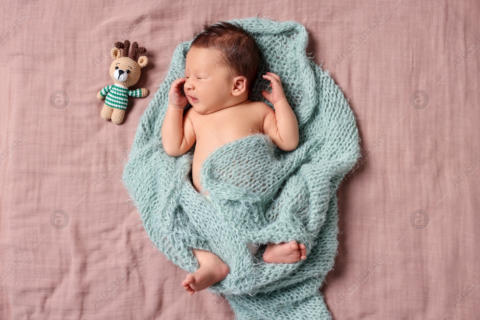 Photo of Cute newborn baby with toy deer in turquoise knitted blanket lying on bed, top view