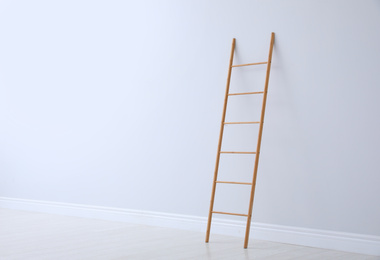 Photo of Modern wooden ladder near white wall. Space for text