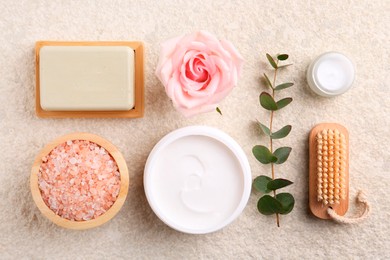 Photo of Flat lay composition with moisturizing cream in open jar and other body care products on light textured table