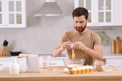 Man making dough while watching online cooking course via tablet in kitchen