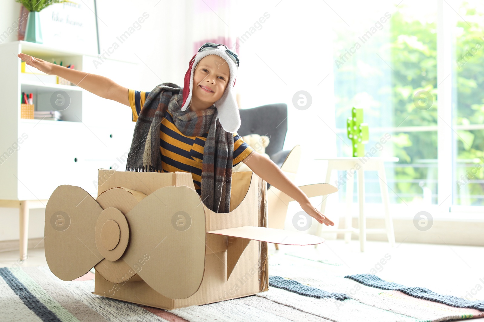 Photo of Adorable little child playing with cardboard airplane indoors