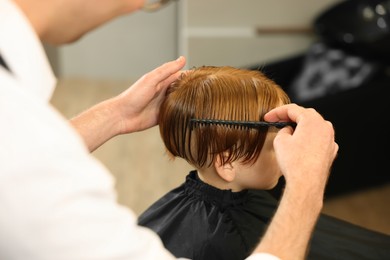 Photo of Professional hairdresser combing boy's hair in beauty salon, closeup