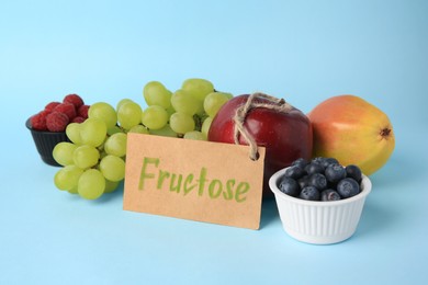 Photo of Card with word Fructose, delicious ripe fruits and berries on light blue background