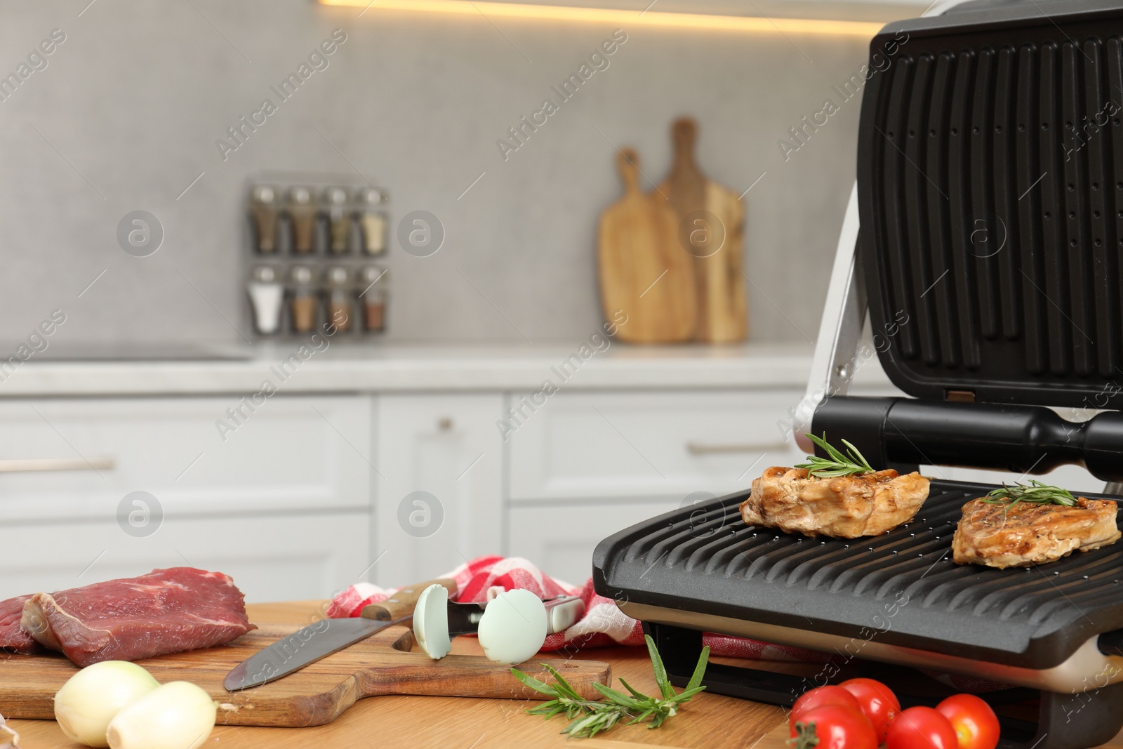 Photo of Electric grill, cooked meat and different products on wooden table, closeup