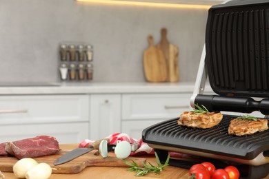 Photo of Electric grill, cooked meat and different products on wooden table, closeup