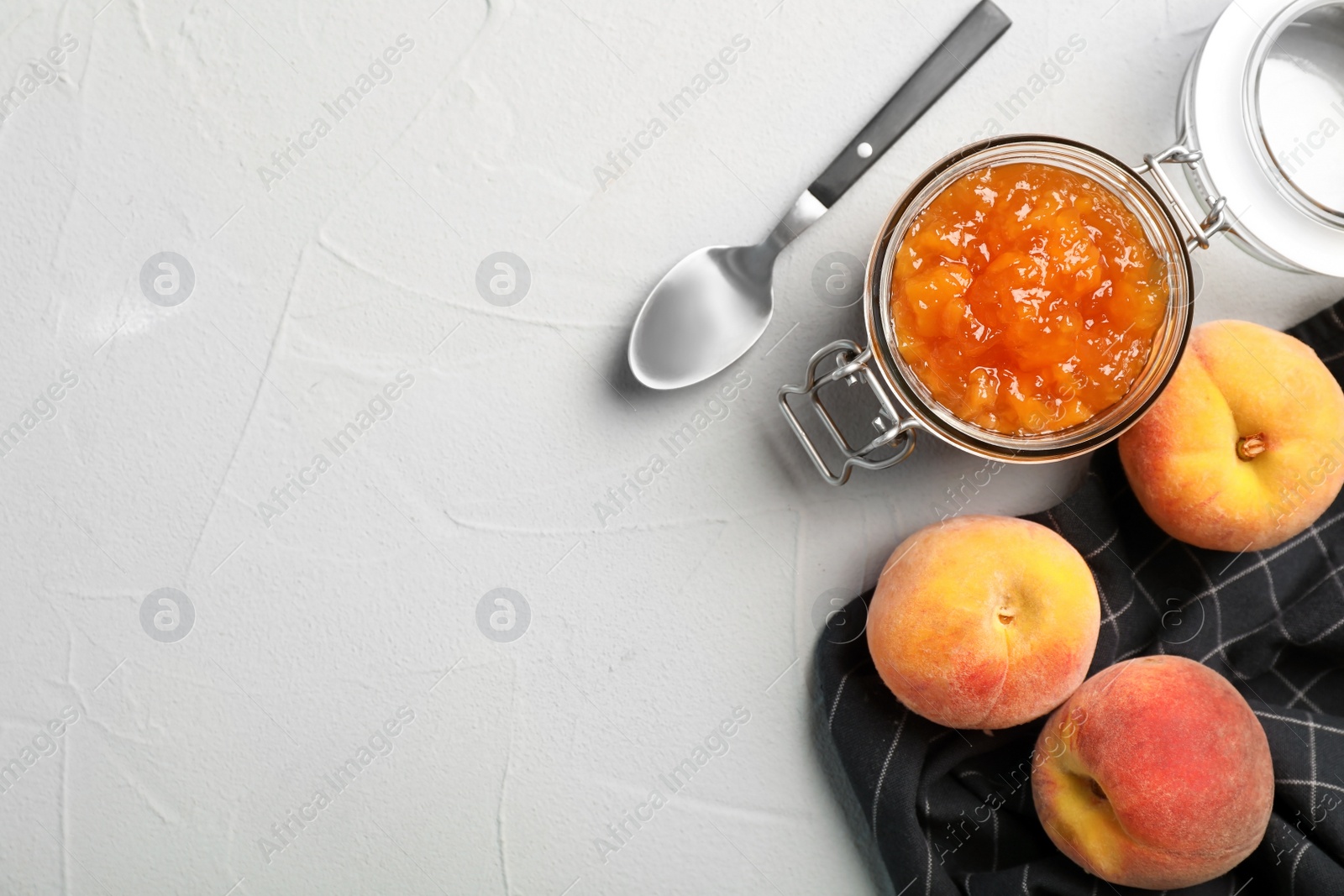 Photo of Flat lay composition with jar of tasty peach jam, spoon and fresh fruit on gray table