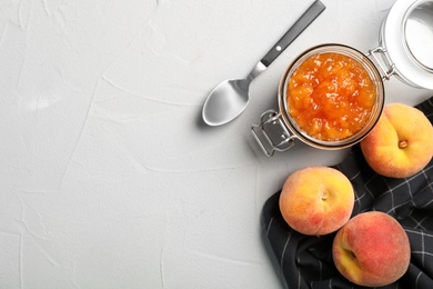 Flat lay composition with jar of tasty peach jam, spoon and fresh fruit on gray table