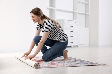Photo of Smiling woman unrolling carpet with beautiful pattern on floor in room