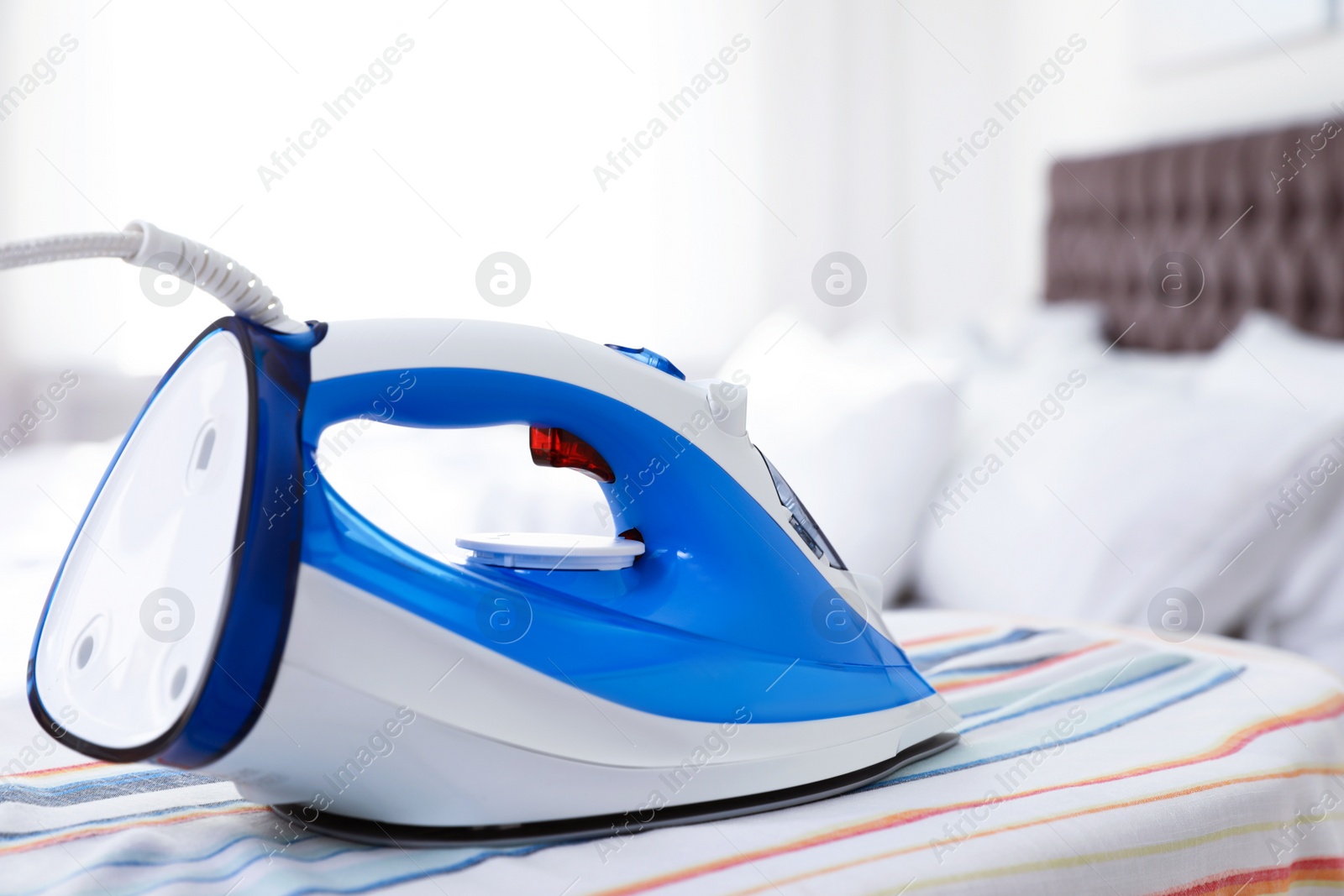 Photo of Modern electric iron on board indoors, space for text. Household appliance