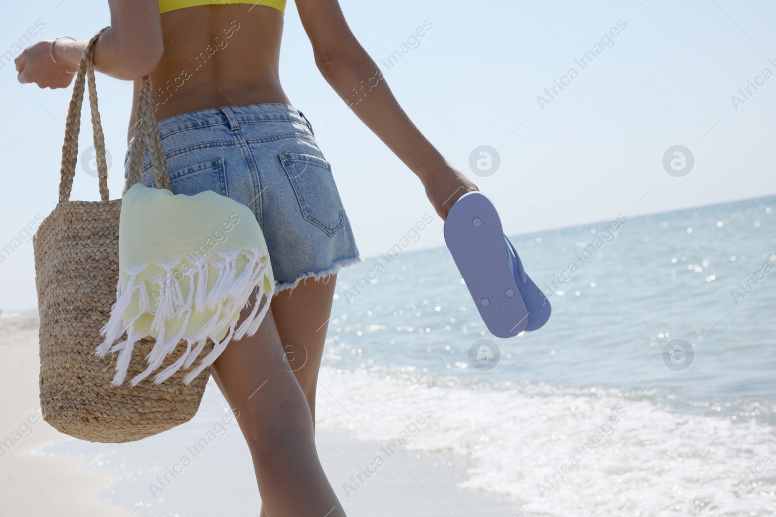 Photo of Woman with beach bag and flip flops walking near sea, closeup