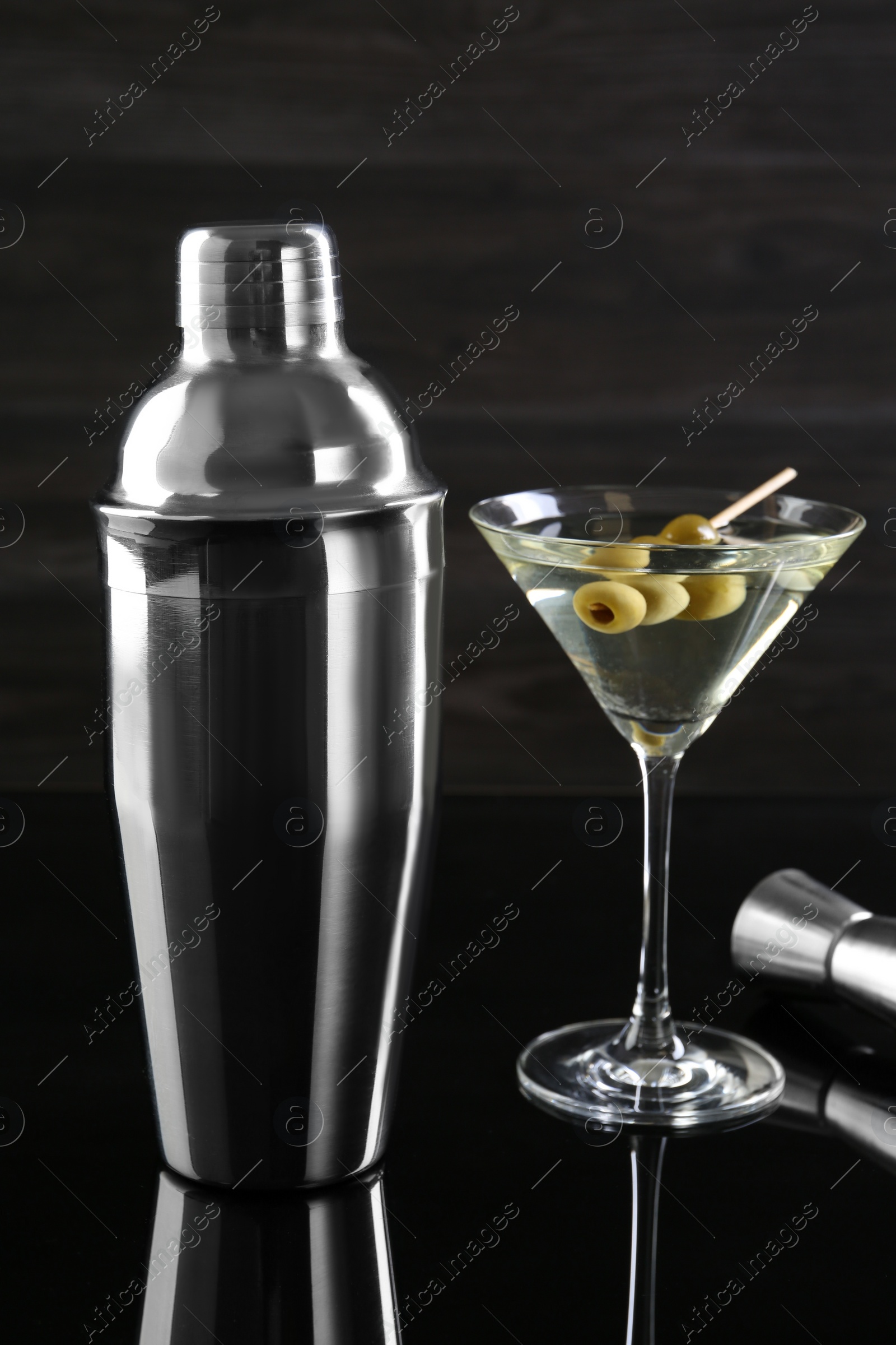 Photo of Metal shaker, Martini cocktail and jigger on black mirror surface