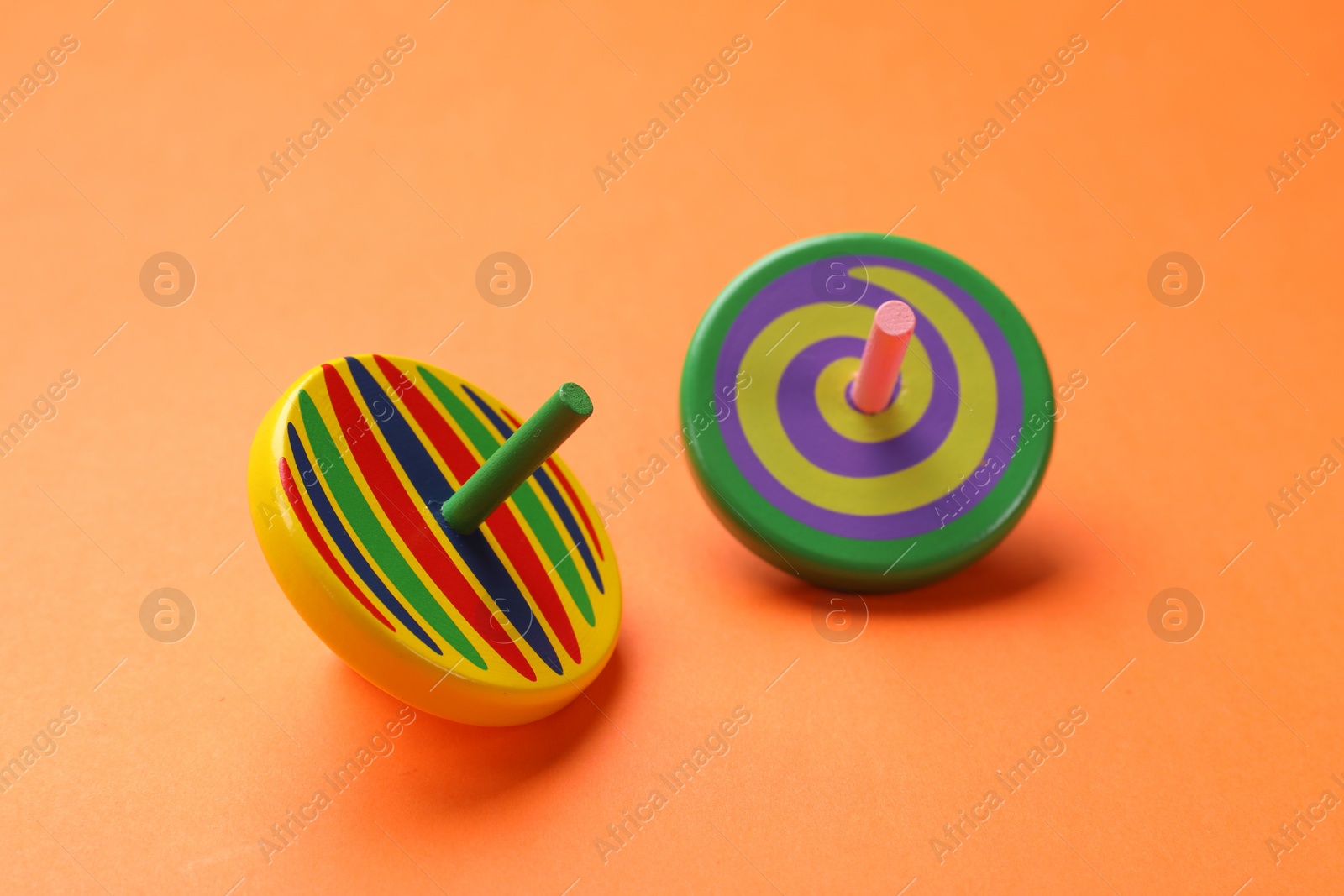 Photo of Two colorful spinning tops on orange background, closeup