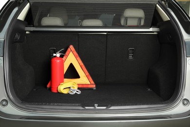 Red fire extinguisher, towing strap and foldable emergency warning triangle in trunk, space for text. Car safety