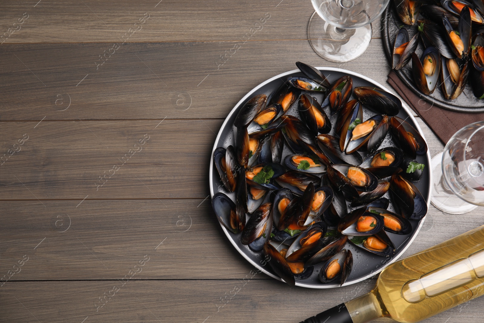 Photo of Cooked mussels with parsley and white wine served on wooden table, flat lay. Space for text