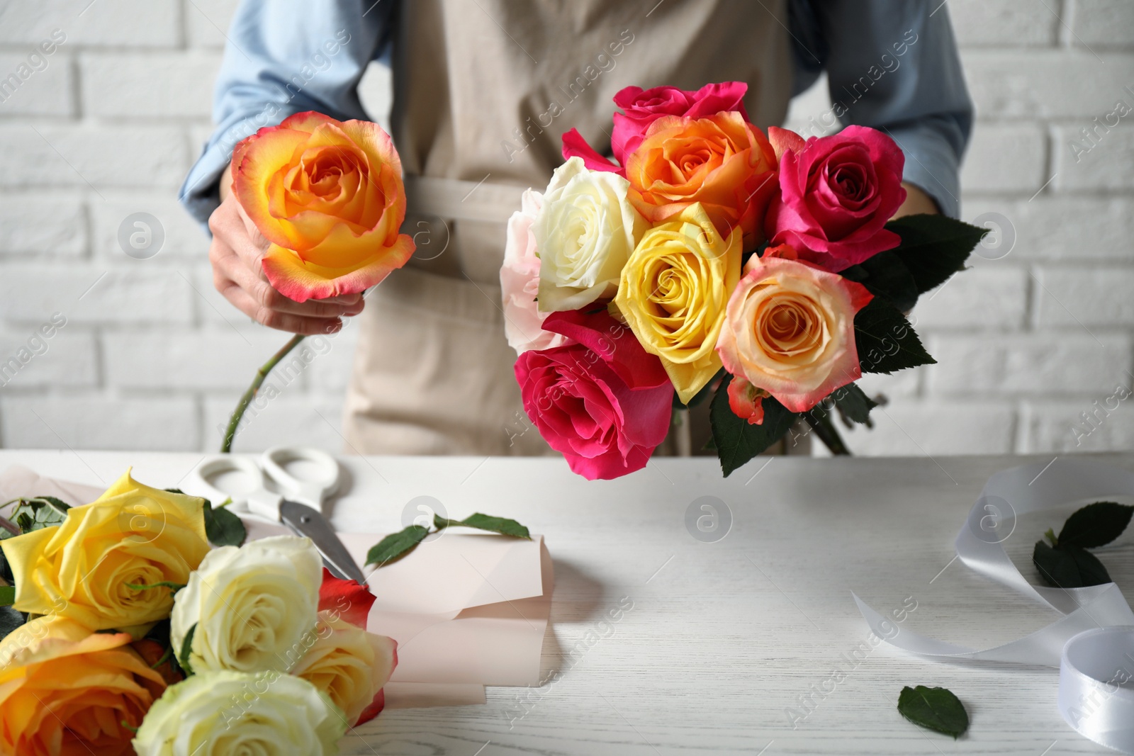Photo of Woman making luxury bouquet of fresh roses at white wooden table, closeup
