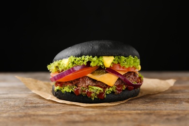 Tasty black burger on table against dark background