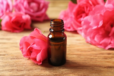 Photo of Bottle of rose essential oil and flowers on wooden table