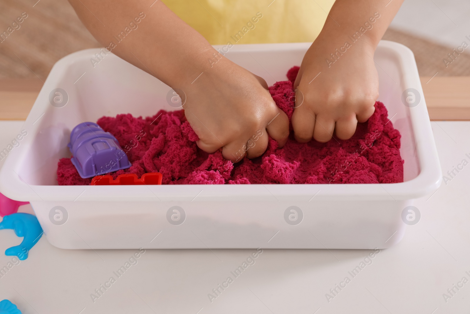 Photo of Little girl playing with bright kinetic sand at table indoors, closeup