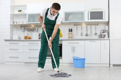 Photo of Male janitor cleaning floor with mop in kitchen