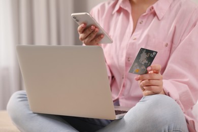 Photo of Woman with credit card using laptop and smartphone for online shopping indoors, closeup
