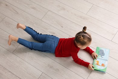 Photo of Cute little girl reading book on warm floor indoors. Heating system