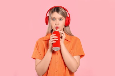 Beautiful woman drinking from red beverage can on pink background