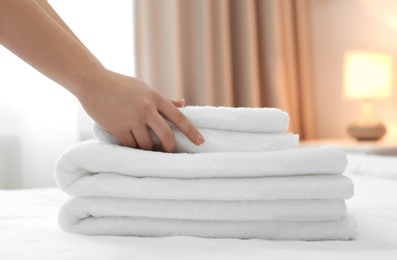 Chambermaid with stack of towels on bed in hotel room