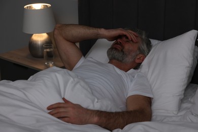 Photo of Mature man suffering from headache in bed at night