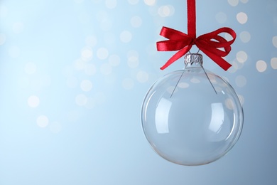 Photo of Transparent glass Christmas ball against light background with festive lights. Space for text