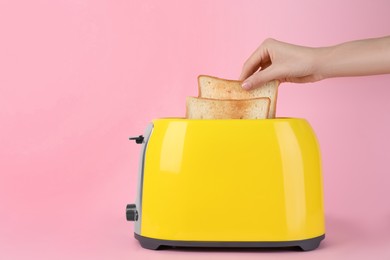 Woman taking slice of bread from yellow toaster on pink background, closeup