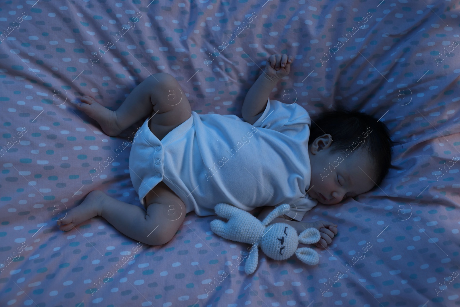 Photo of Cute newborn baby sleeping with toy bunny in crib at night, top view