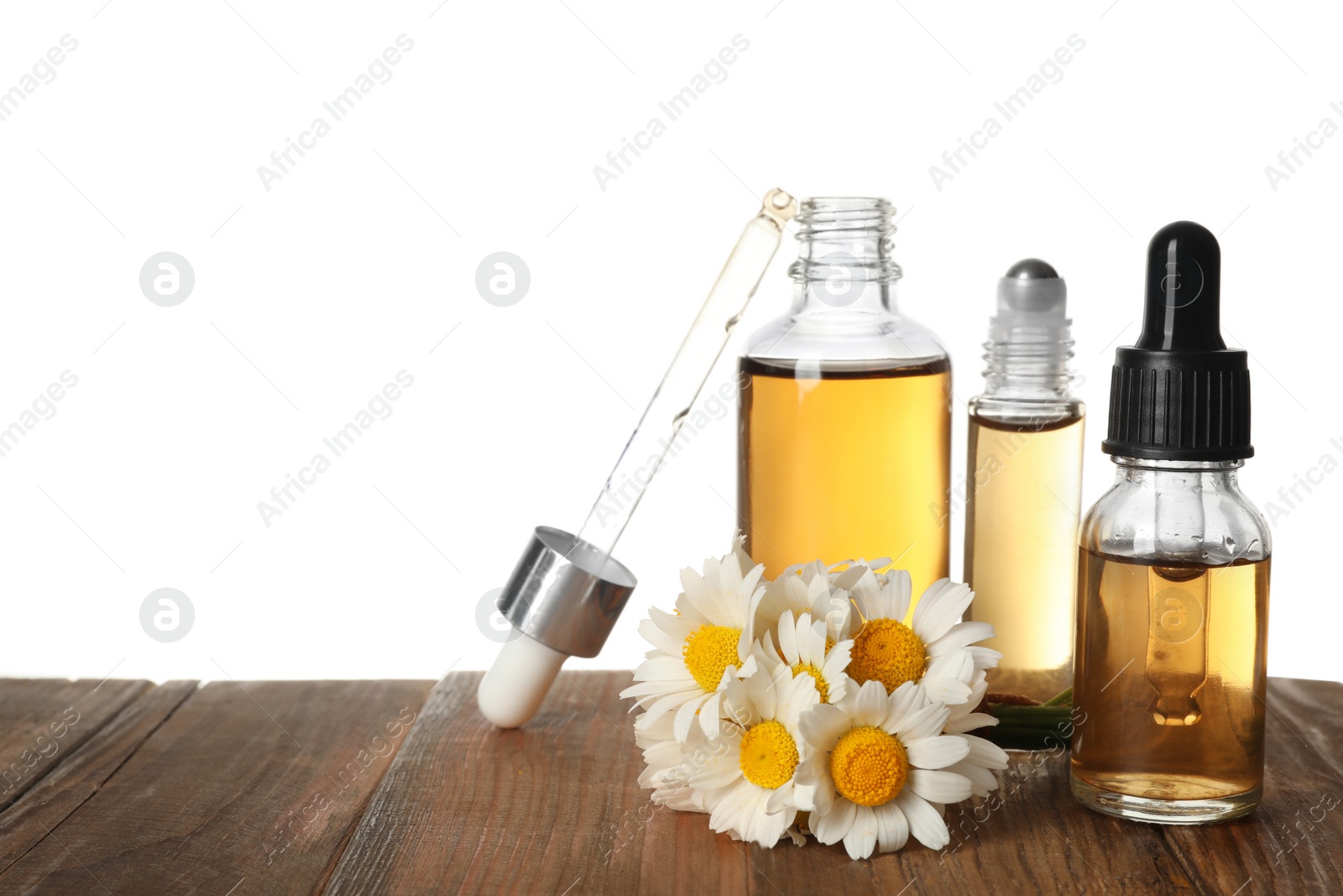 Photo of Chamomile flowers and cosmetic bottles of essential oil on wooden table against white background. Space for text