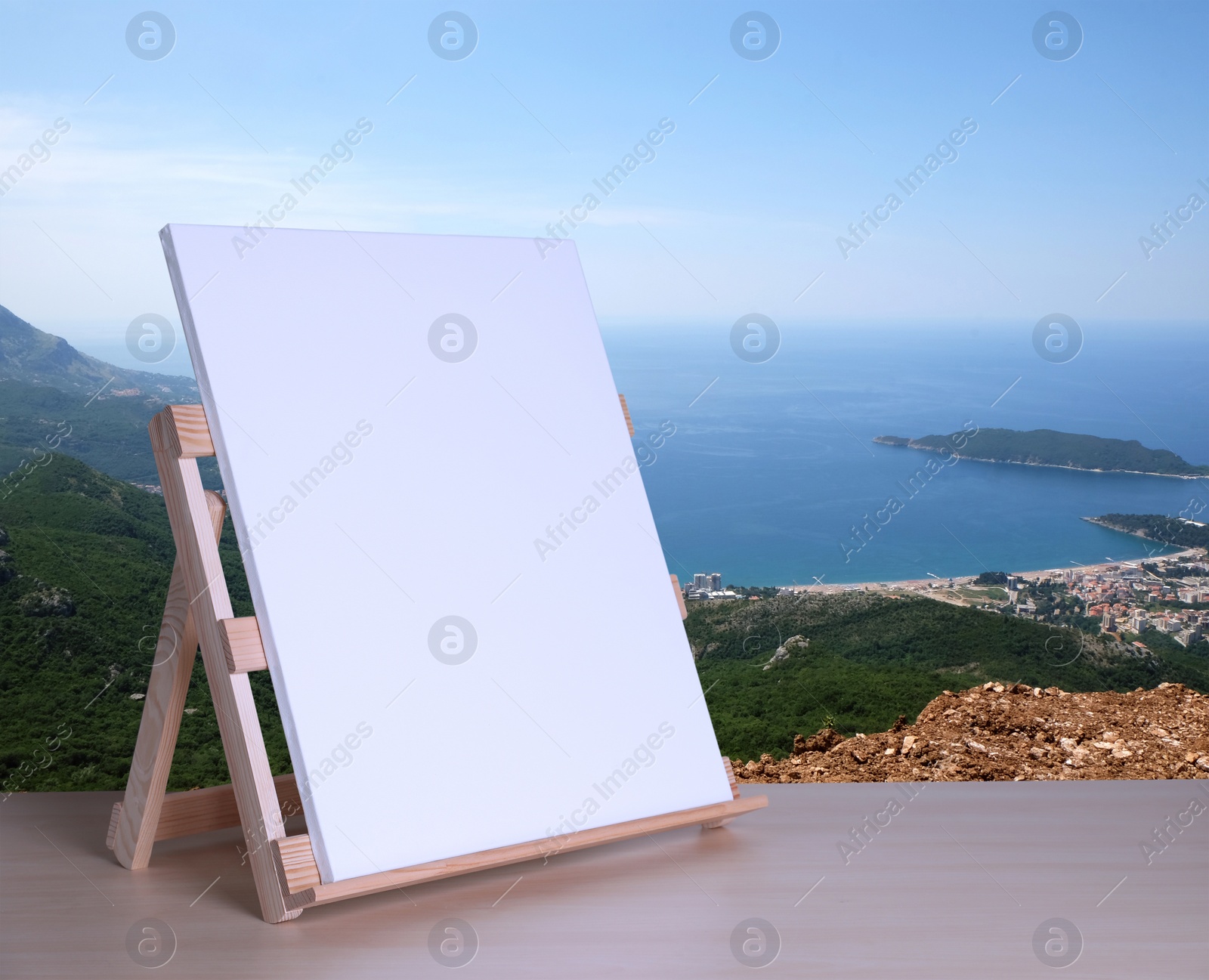 Image of Wooden easel with blank canvas on table and beautiful seascape. Space for text