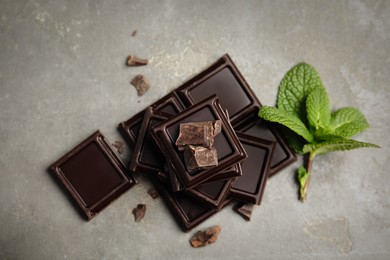 Tasty dark chocolate pieces with mint on grey table, flat lay