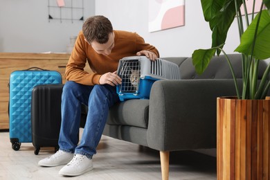 Photo of Travel with pet. Man closing carrier with cat on sofa at home