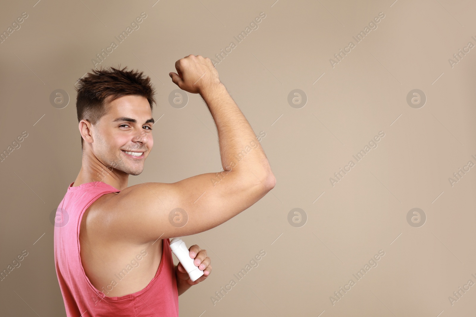 Photo of Young man applying  deodorant to armpit on beige background. Space for text