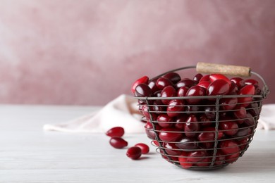 Photo of Fresh ripe dogwood berries in metal basket on white wooden table. Space for text