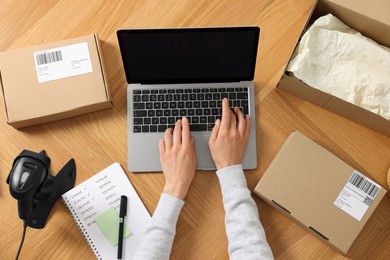 Photo of Woman with laptop working at wooden table, top view. Online store