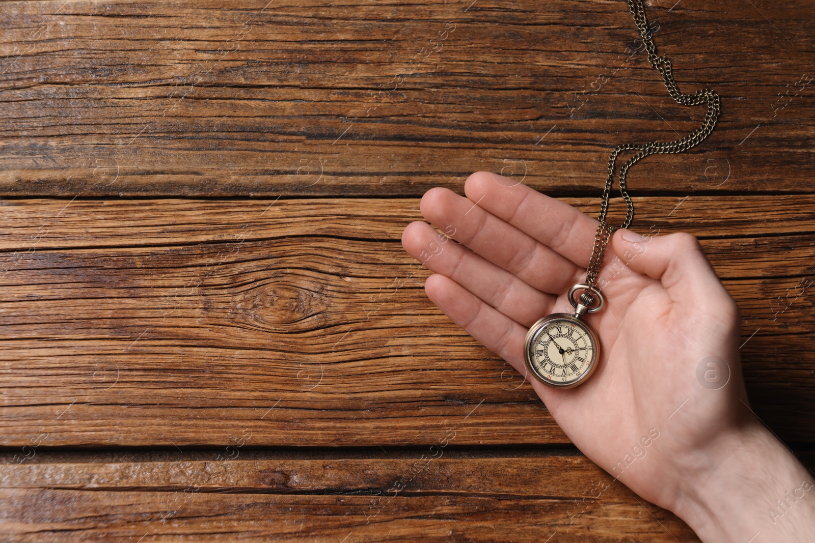 Photo of Man holding chain with elegant pocket watch at wooden table, top view. Space for text