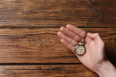 Man holding chain with elegant pocket watch at wooden table, top view. Space for text