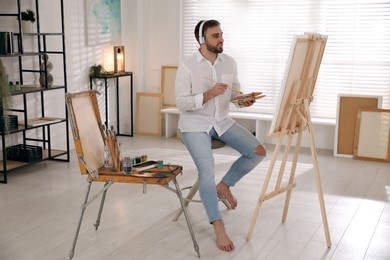 Young man painting on easel with brush in artist studio