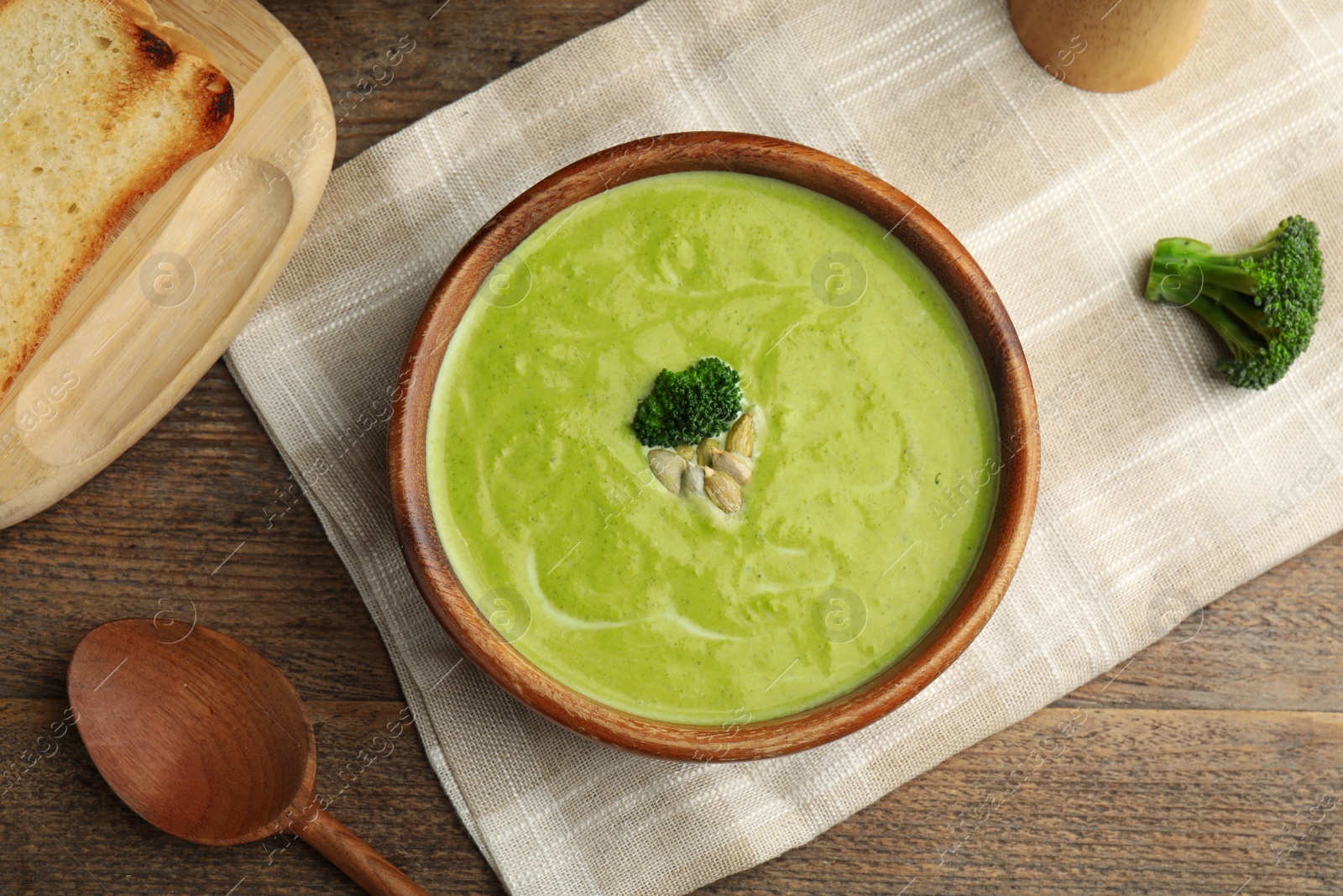 Photo of Delicious broccoli cream soup served on wooden table, flat lay