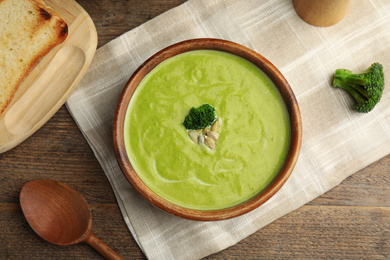 Delicious broccoli cream soup served on wooden table, flat lay