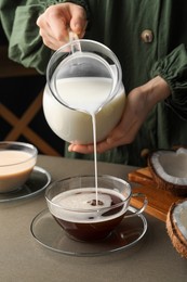 Photo of Woman pouring tasty coconut milk into cup of coffee at table, closeup
