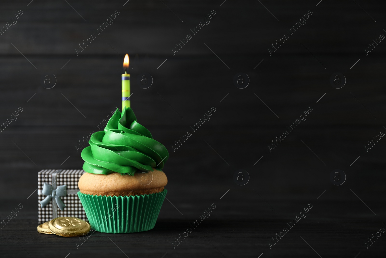 Photo of Decorated cupcake and gift box on black wooden table, space for text. St. Patrick's Day celebration