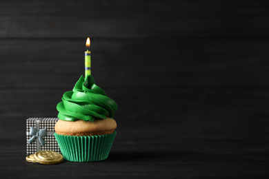 Decorated cupcake and gift box on black wooden table, space for text. St. Patrick's Day celebration