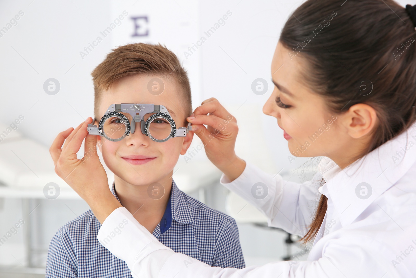 Photo of Children's doctor putting trial frame on little boy in clinic. Eye examination